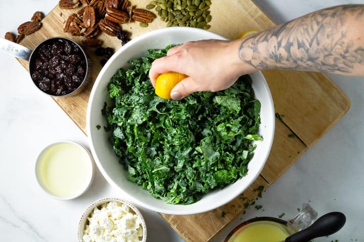Large white bowl filled with chopped kale and lemon juice being squeezed over it