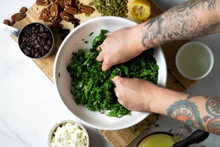 A large white bowl filled with chopped kale being massaged