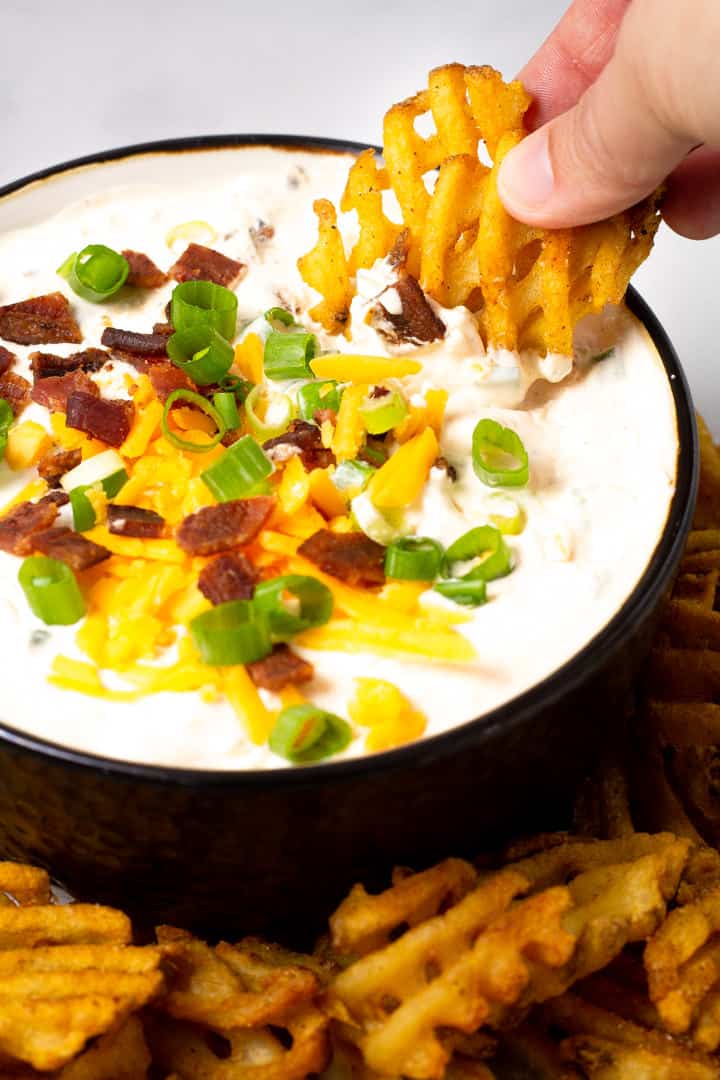 Close up shot of a big bowl filled with loaded baked potato dip with two waffle fries being dipped in it