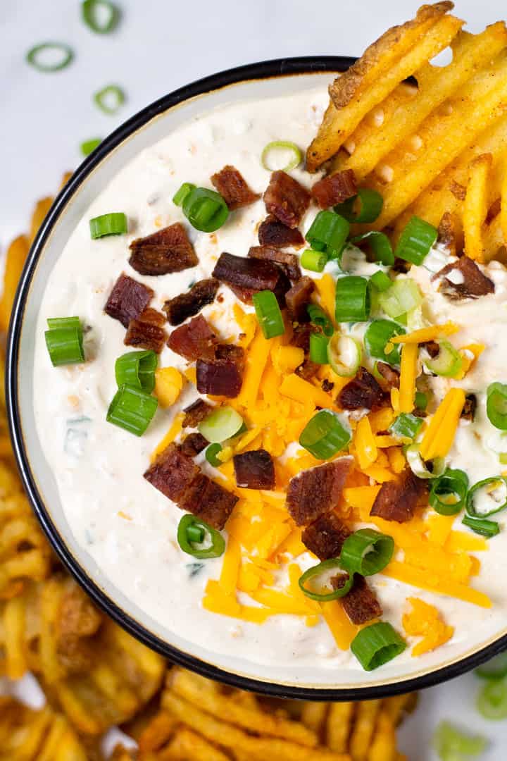 Overhead shot of a big bowl filled with loaded baked potato dip with two waffle fries dipped in it