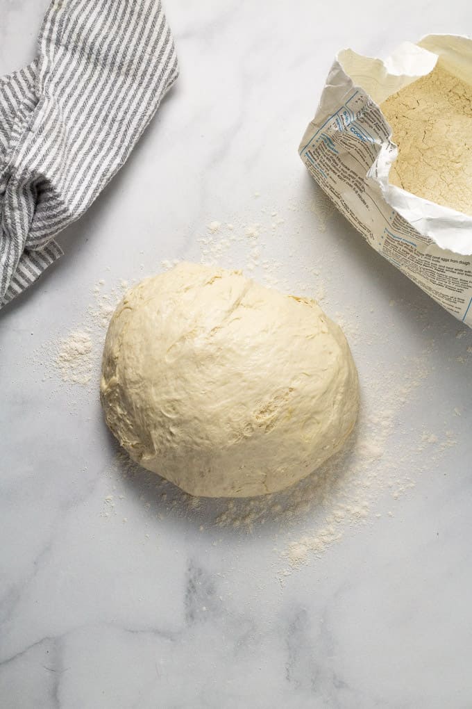 Ball of pizza dough on a white marble counter top dusted with flour