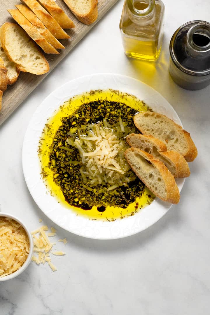 Overhead shot of a plate filled with olive oil and balsamic vinegar dip with Parmesan cheese and herbs