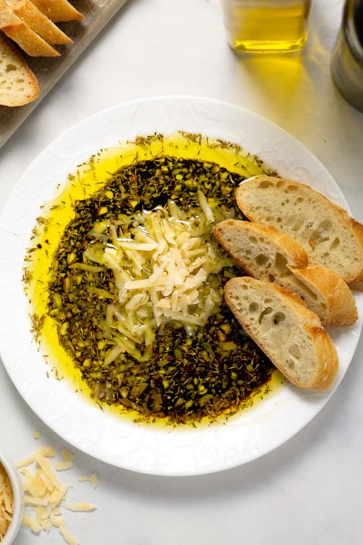 Overhead shot of a plate filled with olive oil and balsamic vinegar dip with Parmesan cheese and herbs