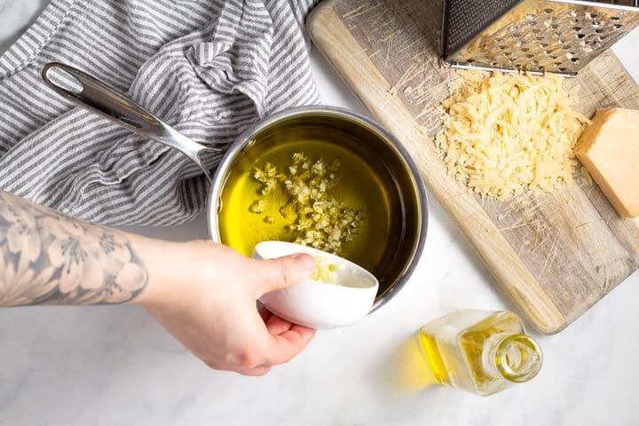 Hand adding minced garlic to the sauce pan of olive oil 