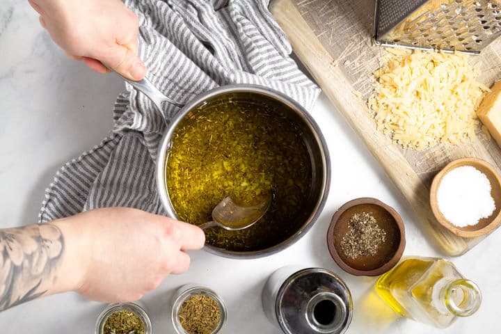 Hand stirring olive oil herbs and garlic in a small saucepan 