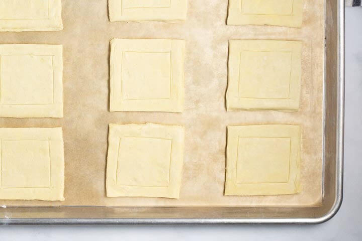 Puff pastry squares on a parchment lined baking sheet