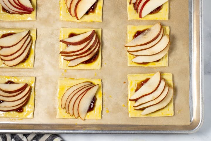 Puff pastry squares with fig jam and pears on a parchment lined baking sheet