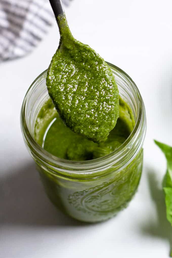 A mason jar of homemade pesto with a spoon coming out of it