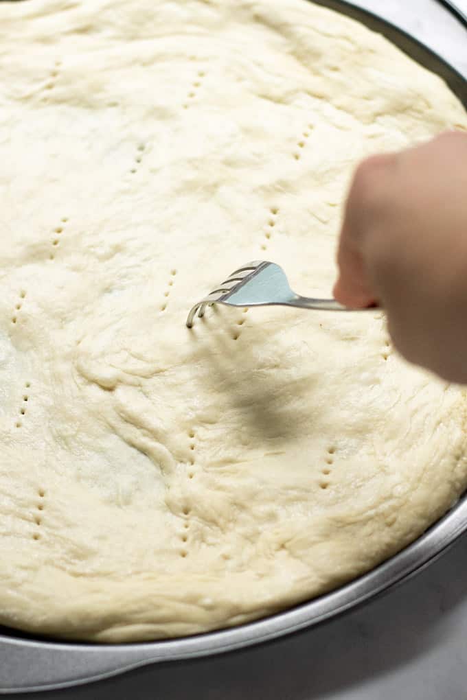 A pizza pan with a pizza crust on top being poked with a fork