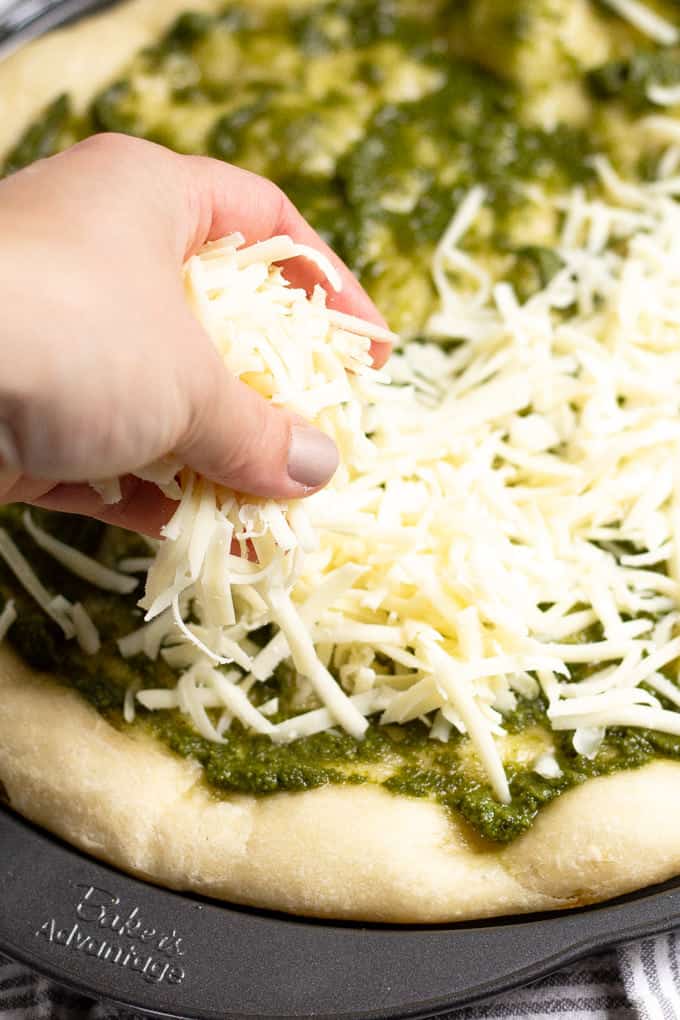 Mozzarella cheese being sprinkled on a pizza crust on a pizza pan