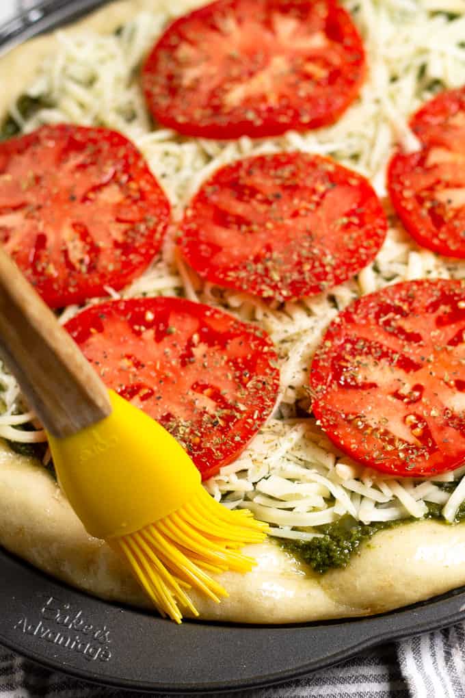 Close up shot of a tomato pizza with the crust being brushed with olive oil 