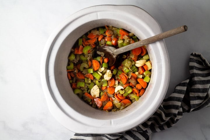 Large crock pot insert filled with carrots celery onion herbs and garlic