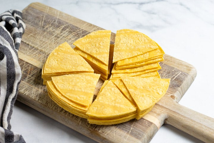 A brown cutting board with corn tortilla triangles on it
