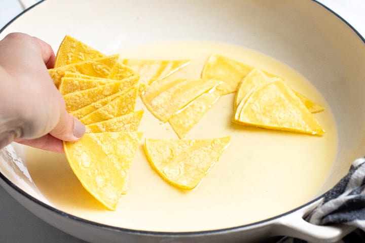 Corn tortilla triangles being added to a pot of shallow oil