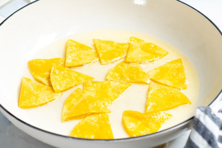 Corn tortilla triangles cooking in a shallow pot of oil