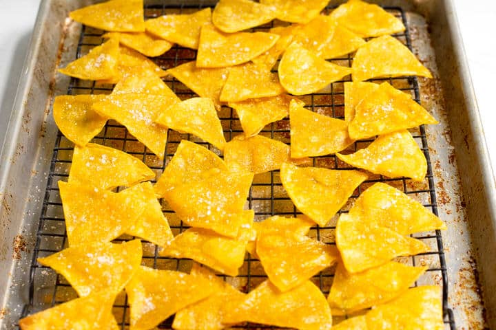 A baking sheet with a cooling rack on it filled with fried corn tortilla triangles