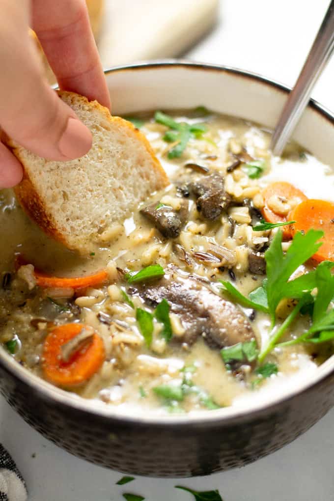 Close up shot of a bowl filled with wild rice soup with bread being dunked in it