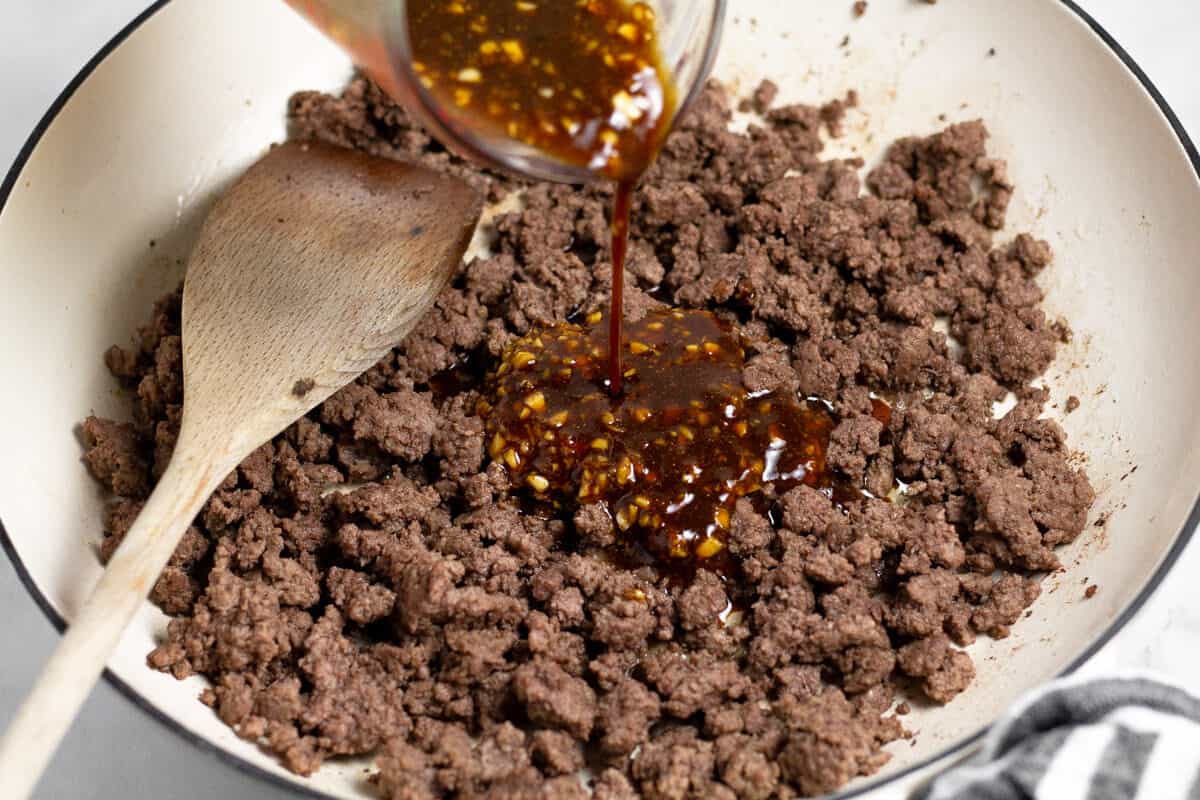 Korean sauce being poured over ground beef in a large white saute pan