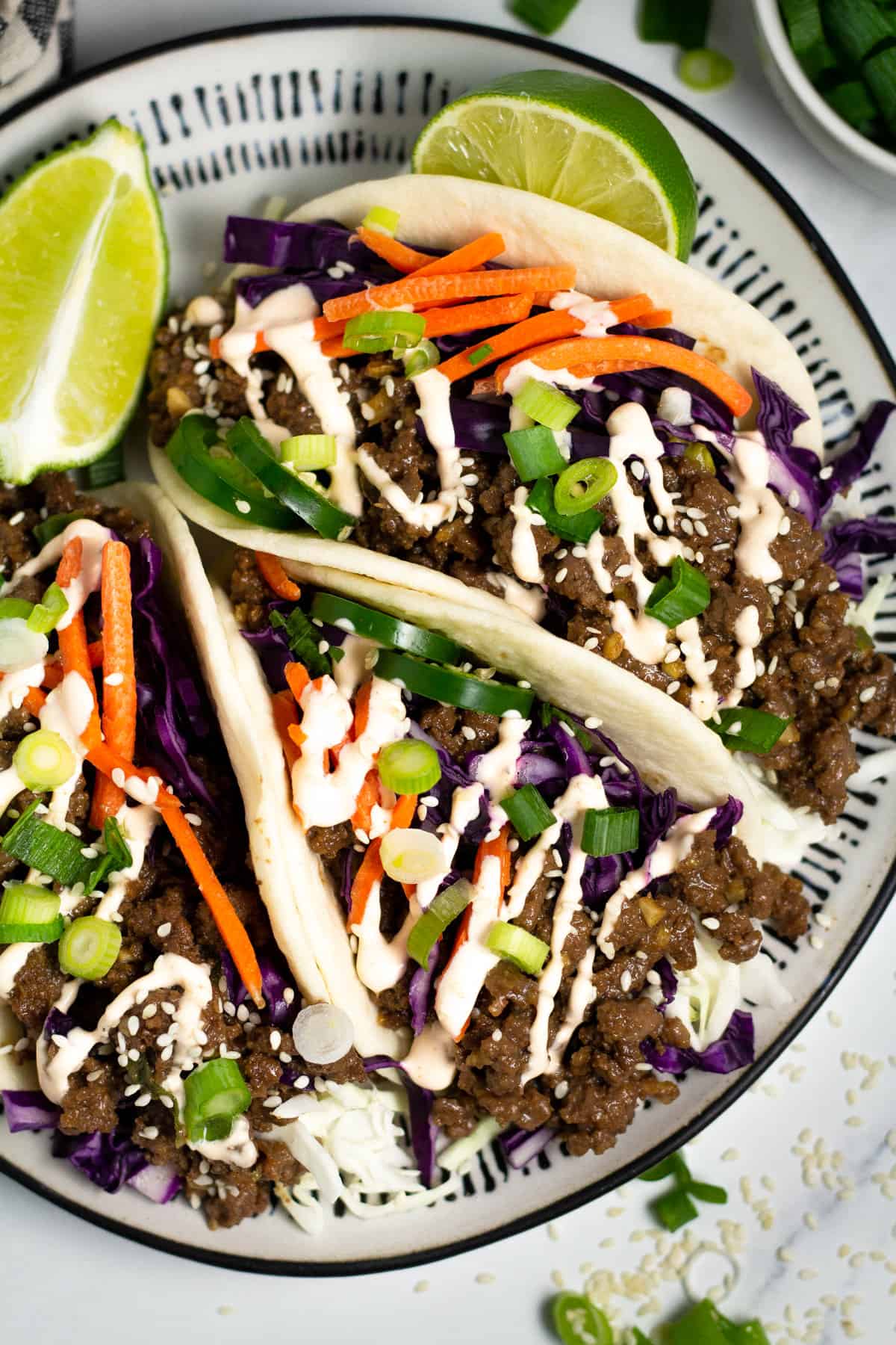 Overhead shot of a black and white plate filled with Korean beef tacos drizzled with spicy mayo.