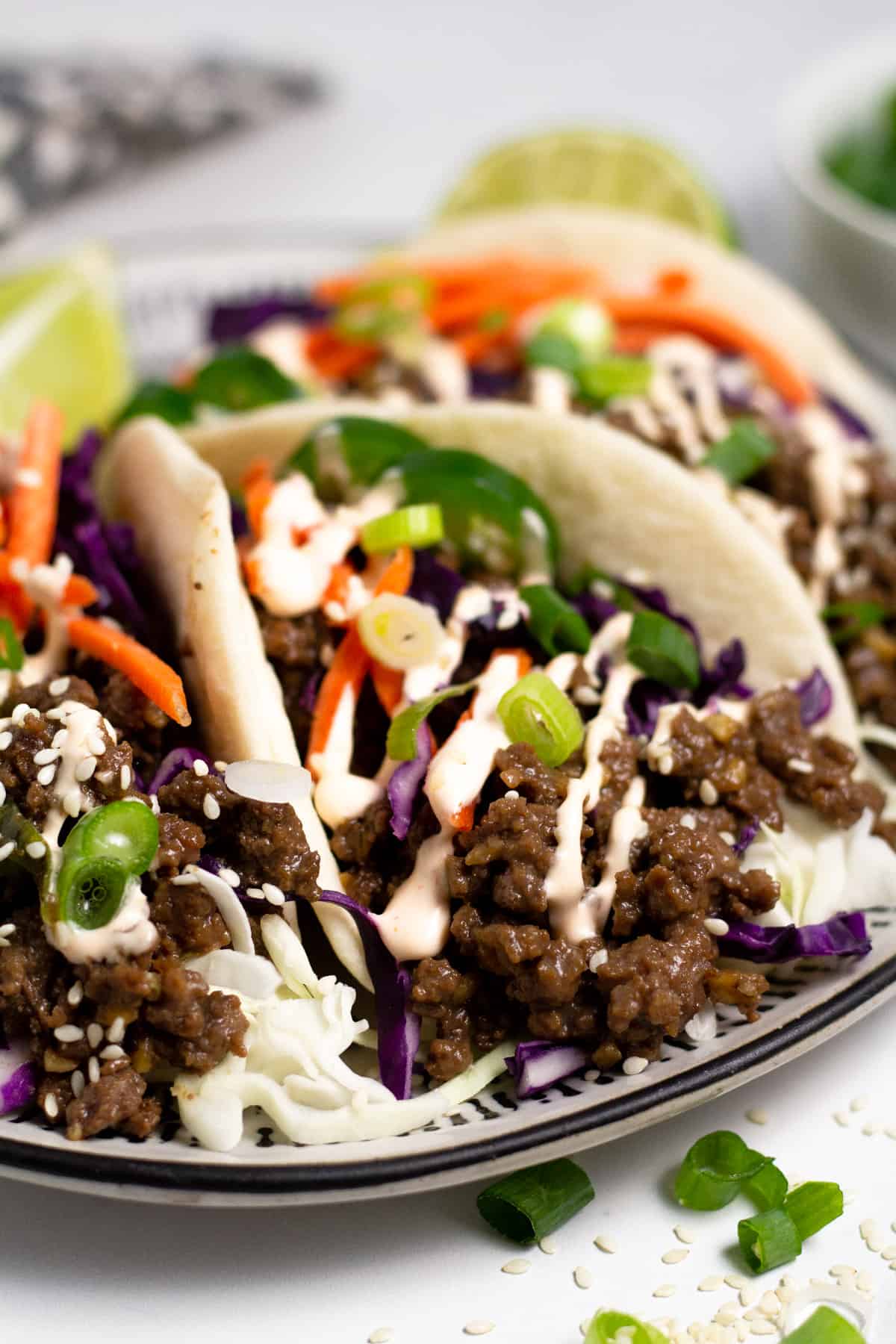 Close up shot of a black and white plate filled with Korean beef tacos drizzled with spicy mayo.
