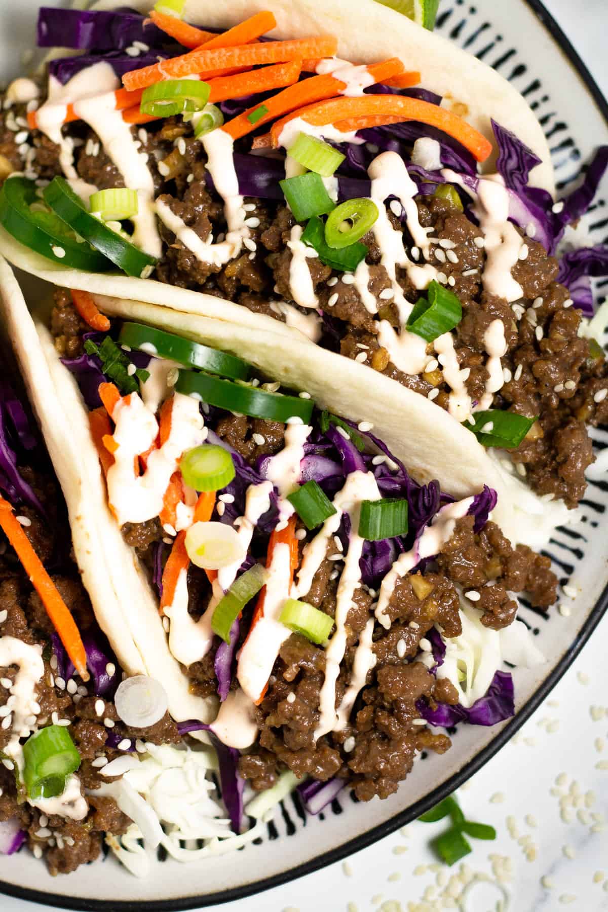 Overhead shot of a black and white plate filled with Korean beef tacos drizzled with spicy mayo.