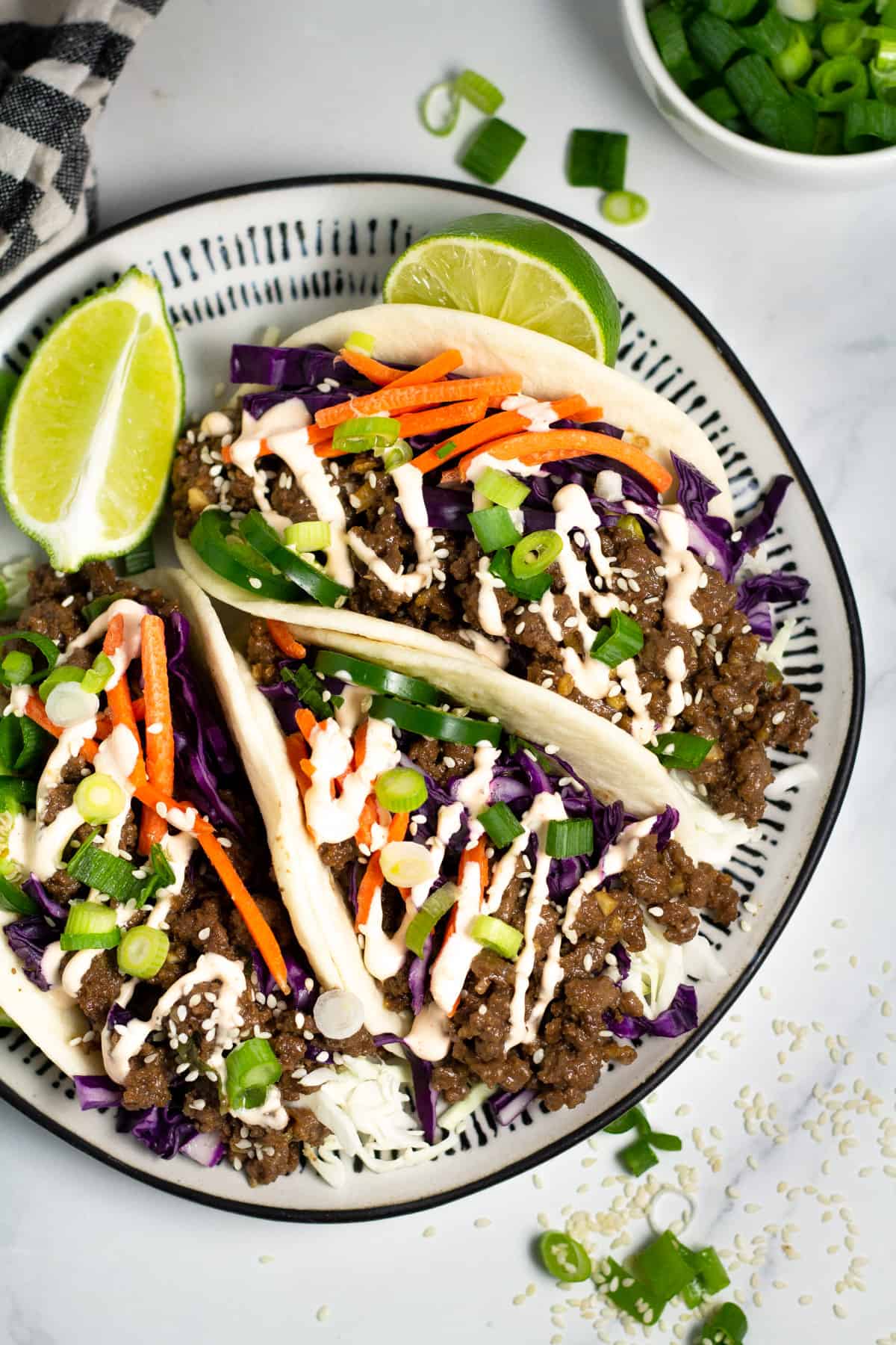 Overhead shot of a black and white plate filled with Korean beef tacos drizzled with spicy mayo.