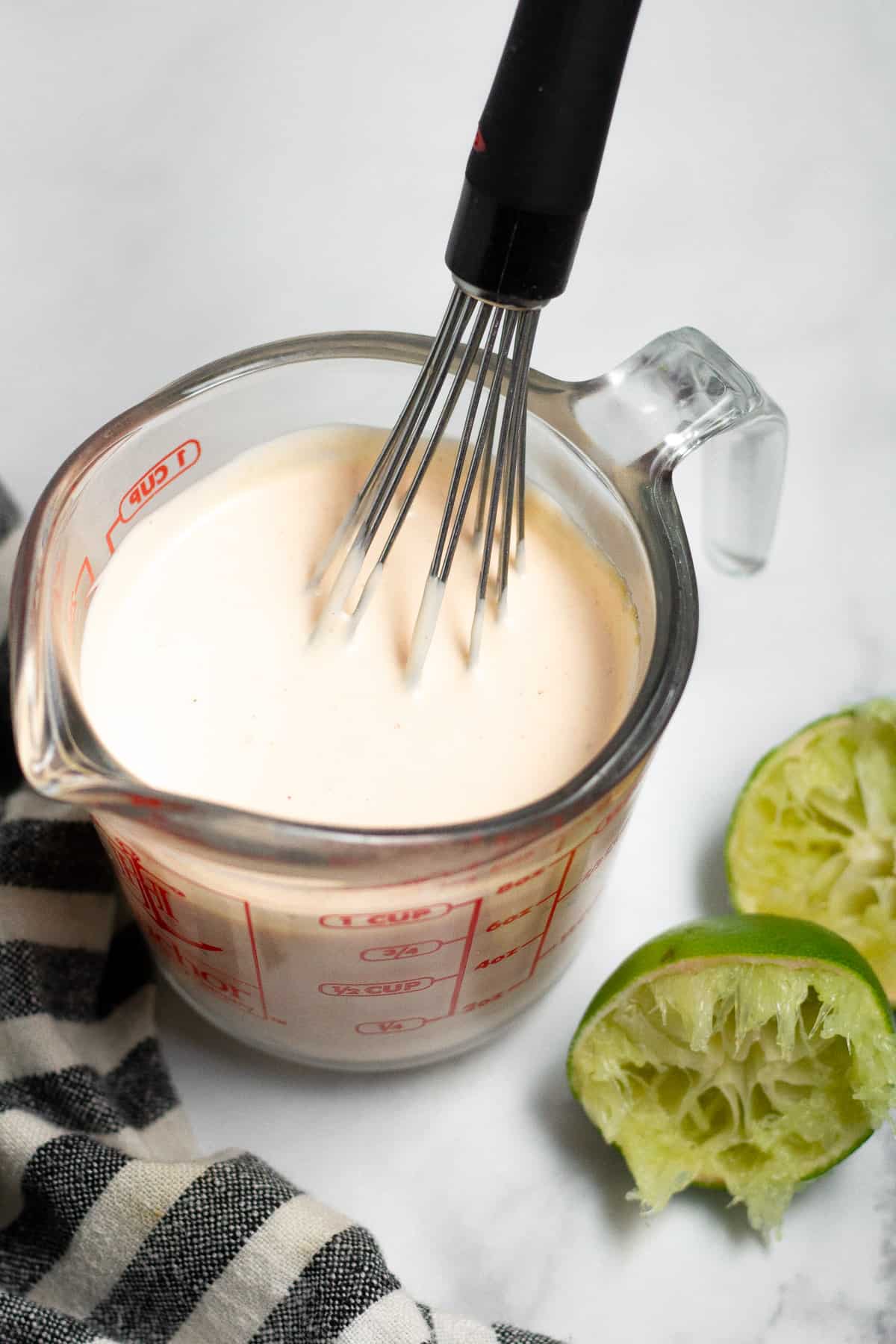 Close up shot of a sriracha mayo sauce in a measuring cup with a whisk