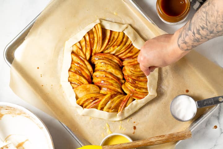 Apple galette on a baking sheet being sprinkled with sugar