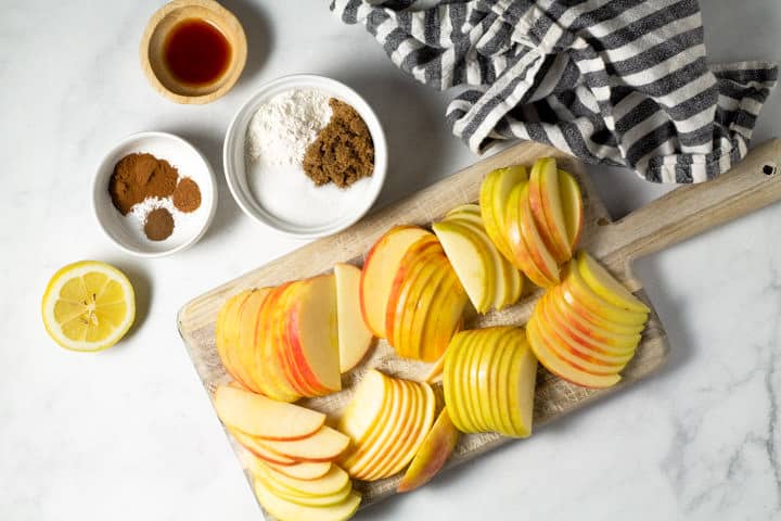 White marble counter top with a cutting board with sliced apples and small bowls of spices
