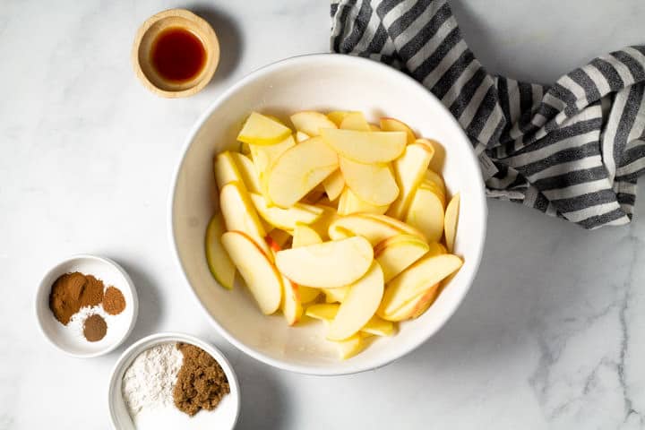 White bowl of sliced apples surrounded by bowls of spices