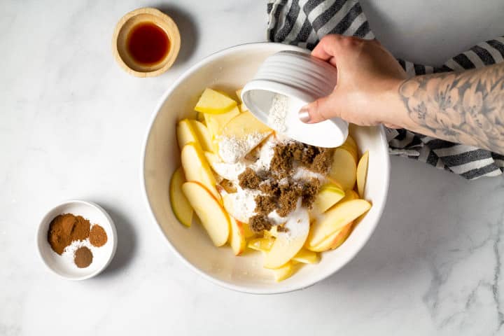 White bowl of sliced apples with spices being added it to it