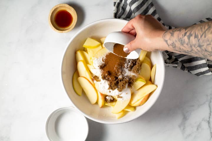 White bowl of sliced apples with spices being added it to it