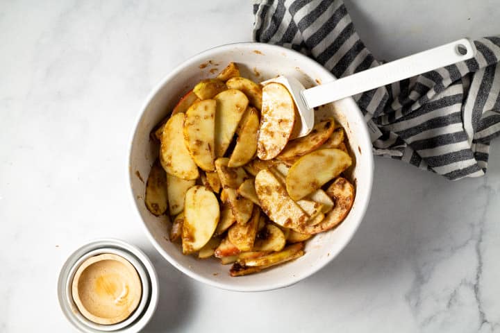 A white bowl filled with sliced apples coated in sugar and spices