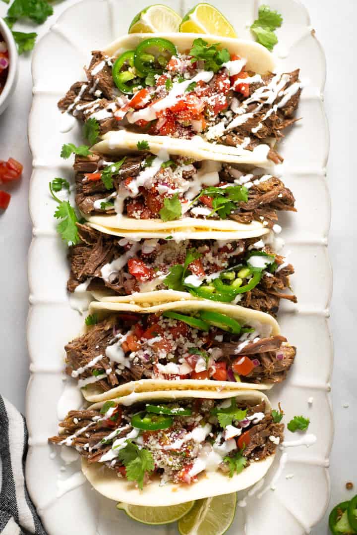 Overhead shot of a white platter filled with barbacoa beef tacos garnished with fresh cilantro