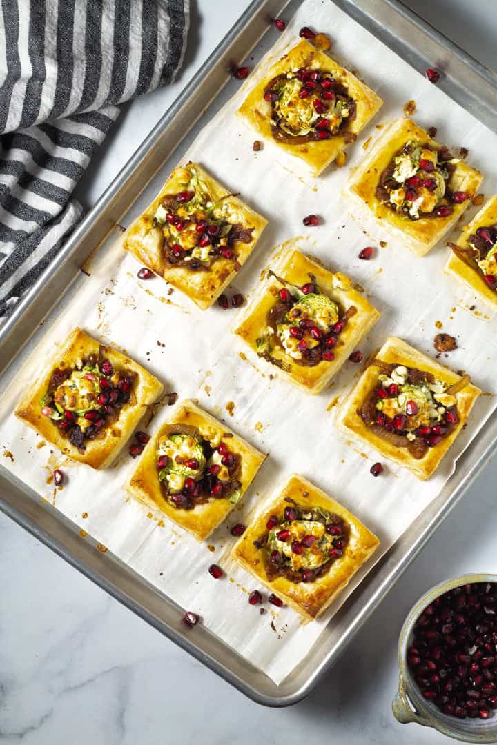 Parchment lined baking sheet with Brussels sprout tarts garnished with blue cheese and pomegranate seeds