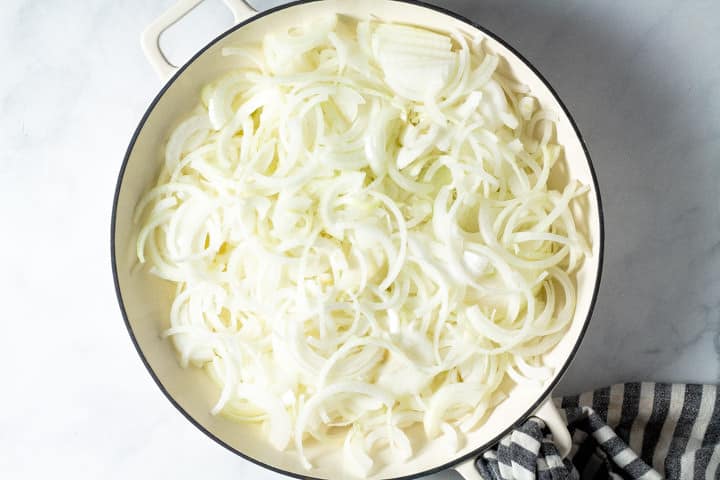 Overhead shot of a white pan filled with thinly sliced onions