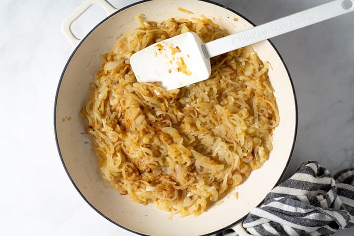 Overhead shot of a white pan filled with thinly sliced onions being caramelized