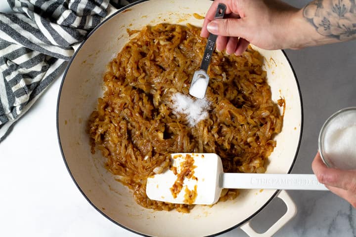 Overhead shot of a white pan filled with caramelized onions with sugar being added to them