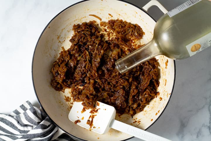 Overhead shot of a white pan filled with caramelized onions with white wine being added to them