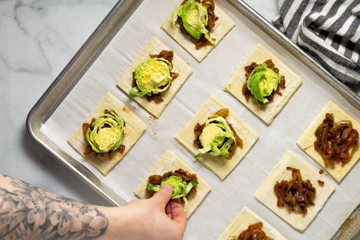 Brussels sprouts being added to puff pastry squares on a baking sheet