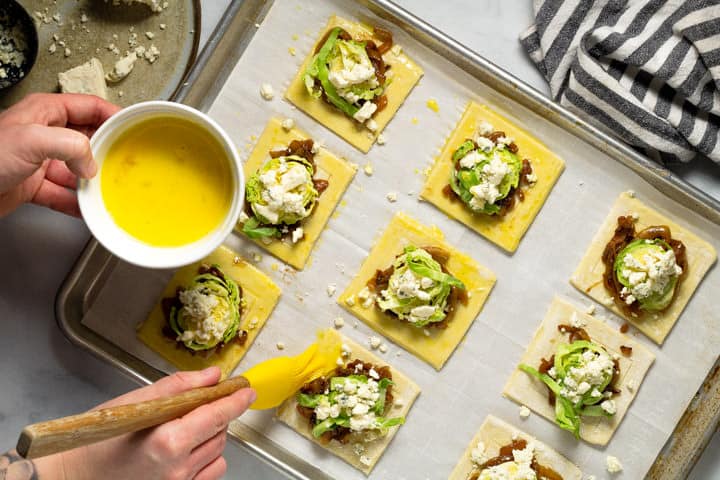 Egg wash being brushed onto the crust of the Brussels sprout puff pastry squares