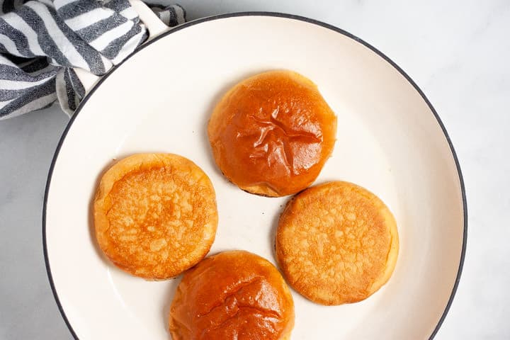 Large white saute pan filled with buns that are browning for burgers