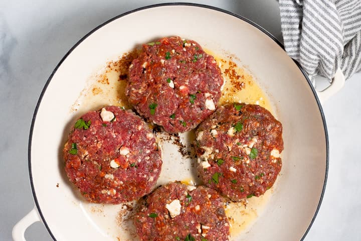 Large white pan filled with Mexican burgers being cooked
