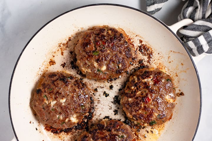 Large white pan filled with Mexican burgers being cooked
