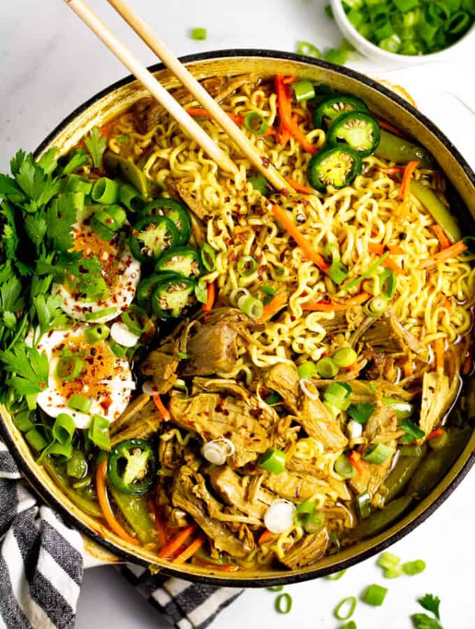 Overhead shot of a large pot filled with curry pork ramen garnished with fresh parsley and sliced jalapenos