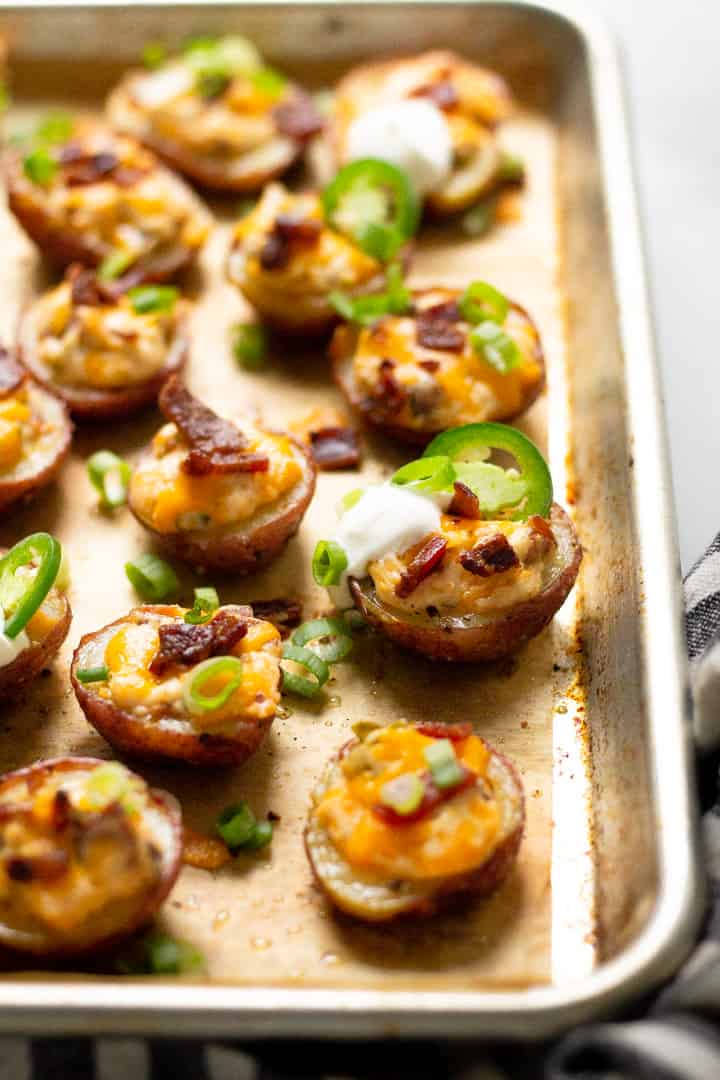 A parchment lined baking sheet with jalapeno popper potato skins garnished with green onion and sour cream 