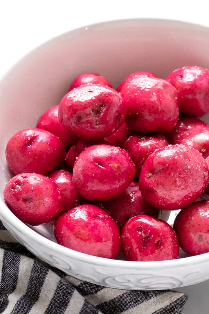 White bowl filled with baby red potatoes in olive oil and sprinkled with salt 