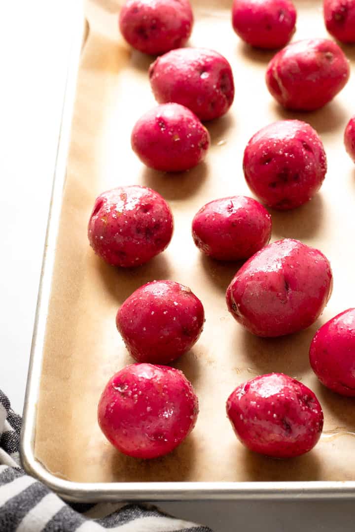 Parchment lined baking sheet with baby red potatoes tossed in olive oil 