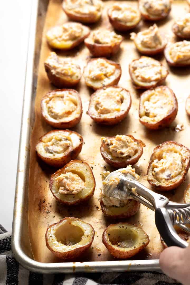 A parchment lined baking sheet with halved baked potatoes with the flesh scooped out of the center being filled with cream cheese filling