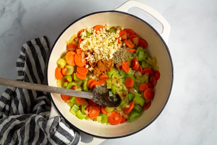 Large white dutch oven filled with vegetables and spices to make lemon orzo soup
